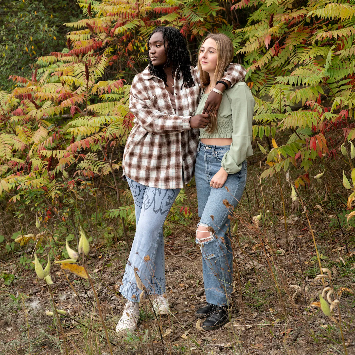 image of two teen girls holding each other in front of fall foliage